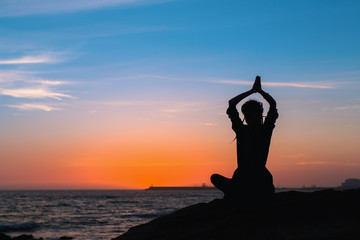 Yoga silhouette of woman meditating in Lotus position on the ocean beach during amazing sunset.