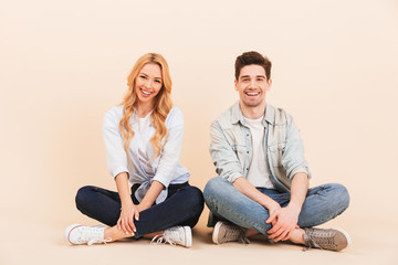 Image of attractive joyful couple man and woman 20s in denim clothing smiling while sitting on the...