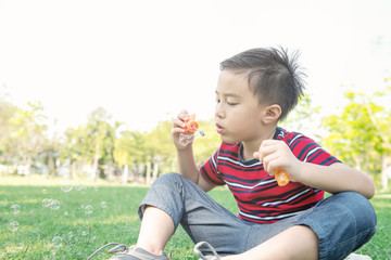 Young boy blowing bubble in park. Chinese boy enjoying playing with his bubble mixture in park.