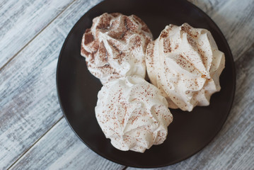 White Meringue Cookies. Sweet Desert over Gray rustic Wooden Board in Black Plate.