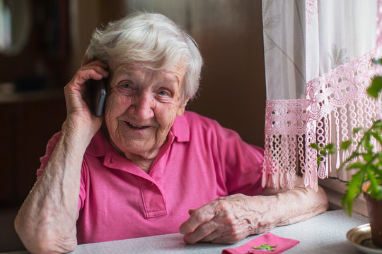 Elderly woman talks on a mobile phone sitting at home.