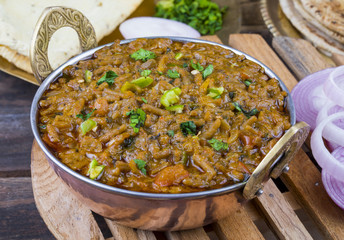 Indian Cuisine Sev Tamatar Also Called Sev Tamaeta or Sev Tameta is Served With Chapati, Papad, Onion or Raita. It is Made With Tomato And Onion Gravy With a Twist of Spicy Sev on Wooden Table