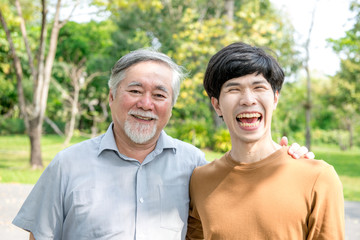 Father and son in park portrait. Retired chinese father with his son holding each other, happy and smiling. Successful family love and relationship concept.