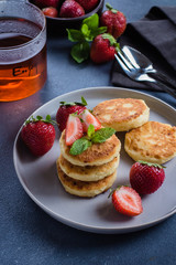 Cottage cheese pancakes with strawberry and cup of tea on blue concrete table background. Breakfast or Lunch Concept