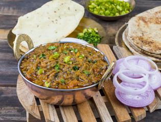 Indian Cuisine Sev Tamatar Also Called Sev Tamaeta or Sev Tameta is Served With Chapati, Papad, Onion or Raita. It is Made With Tomato And Onion Gravy With a Twist of Spicy Sev on Wooden Table