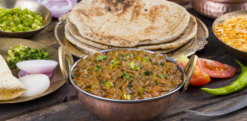 Indian Cuisine Sev Tamatar Also Called Sev Tamaeta or Sev Tameta is Served With Chapati, Papad, Onion or Raita. It is Made With Tomato And Onion Gravy With a Twist of Spicy Sev on Wooden Table