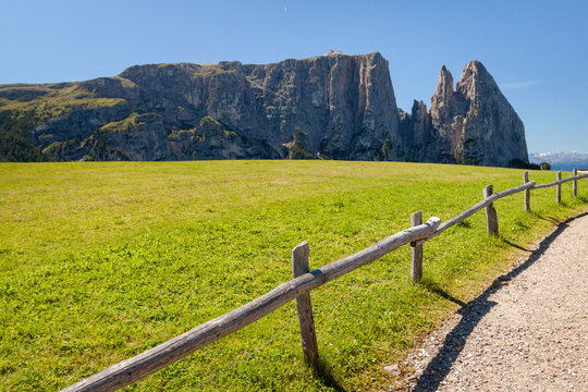 A road with handrails running along a path with dolomite mountains in the background in Seiser Alm - Alp de suise Italy