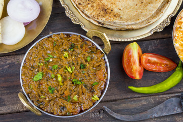 Indian Cuisine Sev Tamatar Also Called Sev Tamaeta or Sev Tameta is Served With Chapati, Papad, Onion or Raita. It is Made With Tomato And Onion Gravy With a Twist of Spicy Sev on Wooden Table