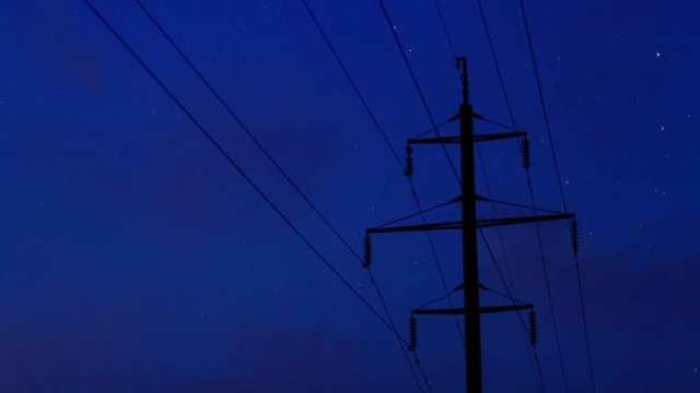 Power line support against the background of the evening starry sky. The sky turns into night and several stars appear. Time laps. The camera approaches the power line support