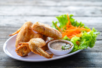 Fried chicken in a white dish with vegetables and dipping sauce on a wooden table.