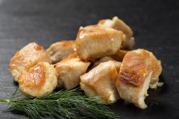 Pieces of fried chicken breast meat on a dark slate with green dill