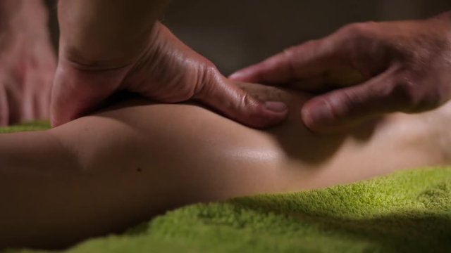 Detail of hands working with human calf muscle. Two therapist applying pressure on female legs in spa salon. Professional male masseuses massaging foot of girl.