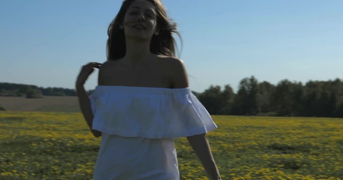 Attractive Young Woman Walks through the meadow and looks at Camera. Outdoor lifestyle portrait. 4K video shooting by handheld gimbal