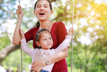 Happy asian mother and her daughter lying on swinging in the garden with rays of sunlight.