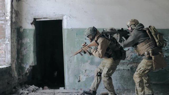 Soldiers in camouflage with combat weapons sneak along the corridors of the old building, the military concept