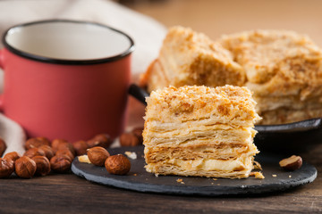Slices of sweet classic layered cake Napoleon, metal mug and hazelnuts 
