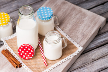 Milk jars with colorful caps on a cutting board, cinnamon and drinking straw 