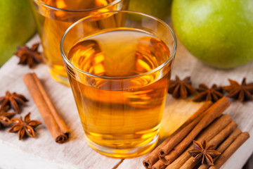 Apple juice in glasses, spices and apples on wooden cutting table 