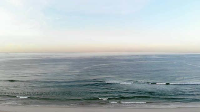 Drone footage of beach at sunrise with small stand up padle riding at sea.