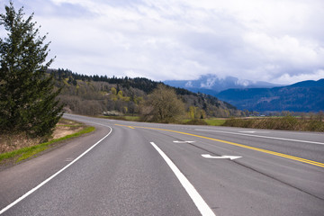 Wide multi-lane road with markings passes through picturesque Columbia Gorge area with meadow forest and mountain