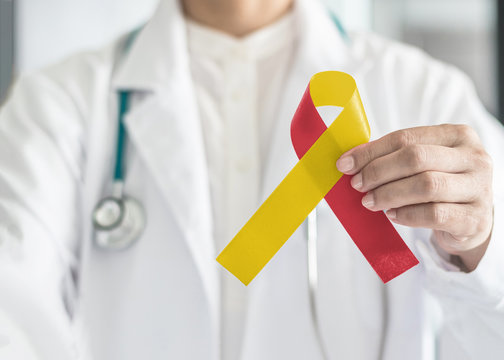 World hepatitis day and HIV/ HCV co-infection awareness with red yellow ribbon in medical doctor hand symbolic bow color to support patient with illness and hepatic disease