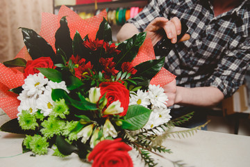 Workplace florist, man collects modern bouquet of hands of roses and white chrysanthemums, holds in hands