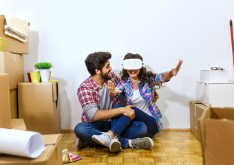 Happy young couple moving into their new home and looking through virtual reality goggles.