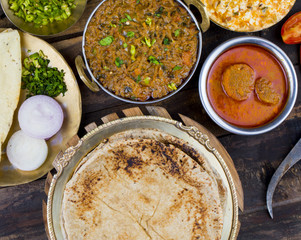 Indian Cuisine in Chapati, Gatta Curry, Sev Tamatar, Raita, Onion or Papad on Wooden Table