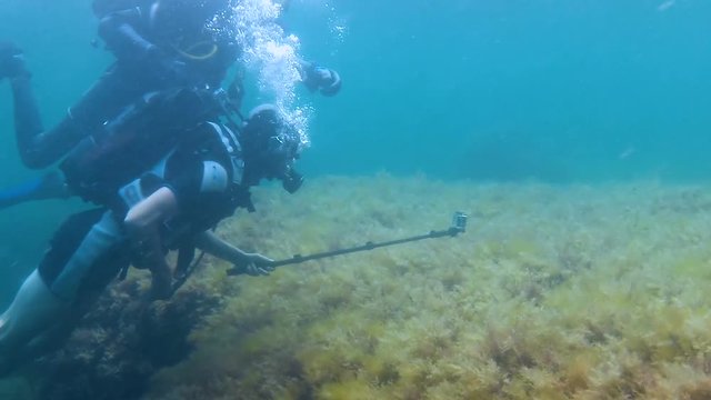 Men in diving equipment moving under water, professional and amateur with camera