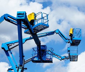 Blue aerial platform of cherry pickers up in the air against blue sky and clouds