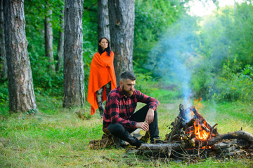 Macho with beer sitting near bonfire, vacation with wife.