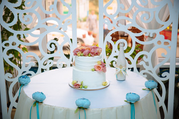 White multilevel wedding cake decorated with pink cream flowers on white table. Candy bar concept