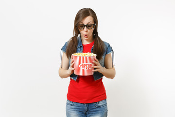 Portrait of funny surprised astonished woman in 3d glasses and casual clothes watching movie film, holding and looking at bucket of popcorn isolated on white background. Emotions in cinema concept.