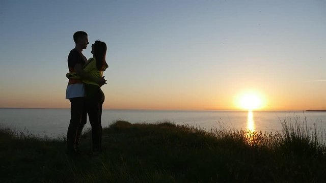 A romantic view of an amorous couple embracing each other and enjoying life at sunset with a golden sun path on the Black Sea shore in summer