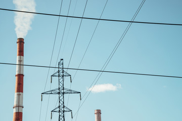 High red and white striped tube lets out white smoke into clear blue sky. Small cloud above pipe on...