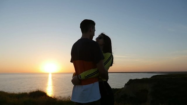 A gorgeous view of a couple in love embracing and looking at each other at sunset with a golden sun path on the Black Sea shore in summer