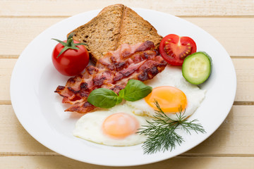 Fried eggs with bacon on the wooden table.