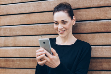 Young smiling woman with smartphone by wooden wall