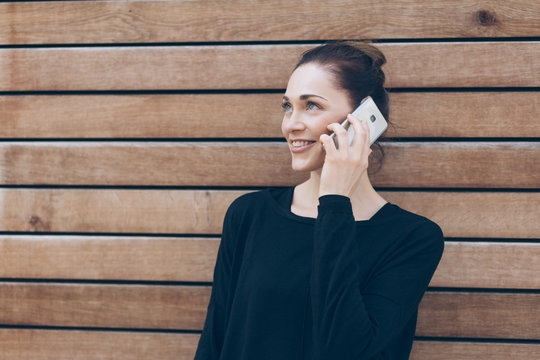 Smiling woman talking on phone against wooden wall