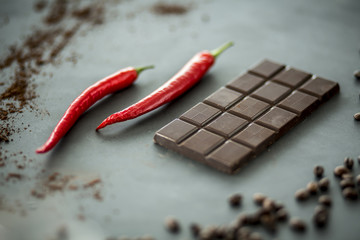 Close-up of hot, red peppers next to a bar of dark chocolate. Mixing flavors concept. Focus in the center and blurred edges,.