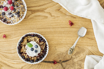 Top view of a wooden breakfast table with two bowls of oatmeal with fruit, elegant silver spoon and white cloth