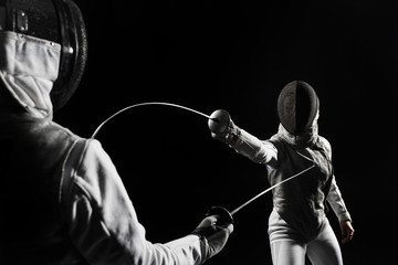 two women wearing helmets and white uniforms fencing on black background