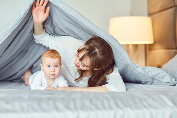 Mother with the baby playing lying on the bed in the bedroom. Mothers Day.