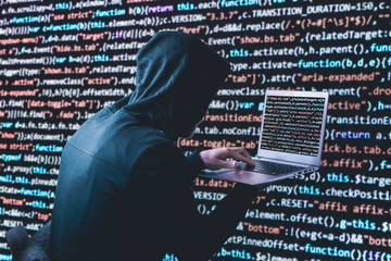 Anonymous hacker with laptop in front of binary code cyber security