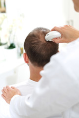 Analiza włosa. Badanie trychologiczne.  Głowa mężczyzny z przerzedzonymi włosami podczas badania skóry głowy i włosów mikroskopem