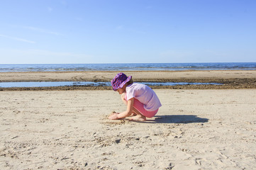 Adorable little girl playing with sand on the beach of Baltic sea.
