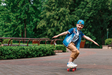 A small city boy and a skateboard. A young guy is riding in a park on a skateboard. City Style. City children. A child learns to ride a skateboard