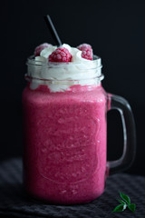 Raspberry smoothie with cream in a mug on a dark background