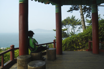 Asian woman resting after jogging; Japanese-style garden house in a park by the sea; Busan (South Korea)