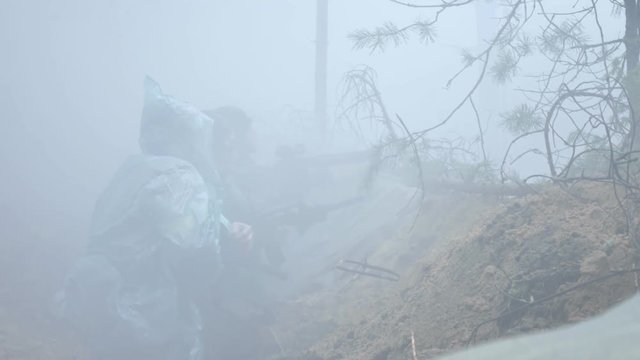Soldiers in camouflage with combat weapons shoot at the forest shelter, military concept, smoke screen, fog